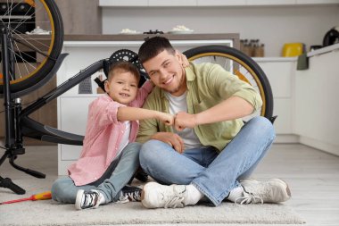 Genç adam ve küçük oğlu evde bisiklet tamir ediyor ve yumruk tokuşturuyorlar.