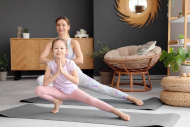Küçük kızıyla birlikte evde minderlerde yoga yapan genç bir kadın.