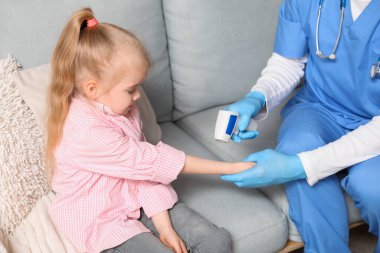 Male pediatrician measuring temperature of little girl with infrared thermometer at home