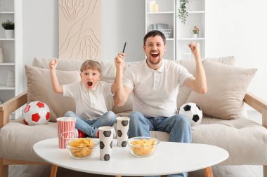 Küçük baba ve küçük oğlu evde futbol takımı için tezahürat yapıyor.