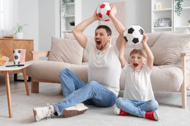 Genç baba ve küçük oğlu futbol toplarıyla evde oturuyorlar.