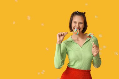 Tatlı lolipopları ve sarı arka planda sabun köpükleri olan genç bir kız.