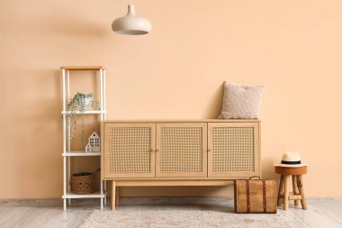 Bej duvarın yanında ahşap çekmeceleri ve raf ünitesi olan rahat oturma odasının içinde.