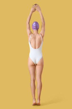 Sarı arka planda poz veren genç bayan yüzücü.