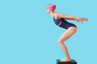 Mavi arka plan ve kenar manzaralı sıçrama tahtasında mutlu genç bayan yüzücü.