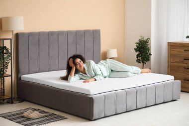 Genç Afro-Amerikalı kadın yatak odasında yumuşak bir yatakta yatıyor.