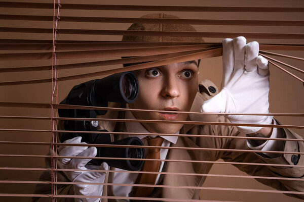 Male spy with binoculars looking through blinds on brown background, closeup