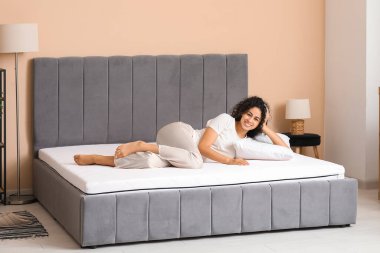 Yatak odasındaki yumuşak yatağın üzerinde yastıklı mutlu Afro-Amerikan kadın.