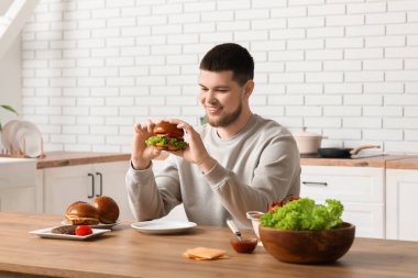 Mutfakta lezzetli burgeri olan genç bir adam.