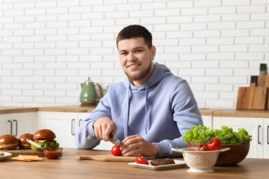 Genç adam mutfakta domates doğruyor.