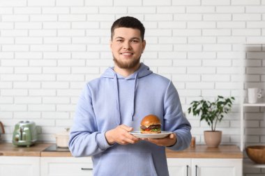 Mutfakta lezzetli hamburgerle tabağı tutan genç adam.