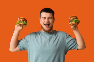 Turuncu arka planda lezzetli burgerleri olan genç bir adam.