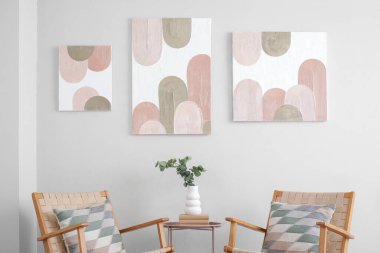 Rahat koltuklar, kahve masası, okaliptüs dallı vazo ve oturma odasındaki beyaz duvarda güzel resimler.