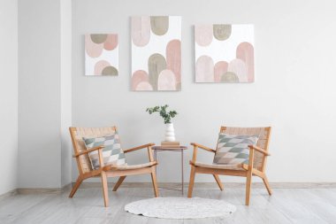 Rahat koltuklar, kahve masası, okaliptüs dallı vazo ve oturma odasındaki beyaz duvarda güzel resimler.