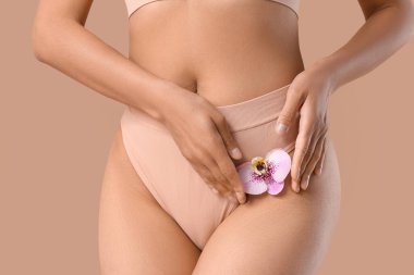 Kahverengi arka planda güzel bir orkide çiçeği olan külotlu genç bir kadın.