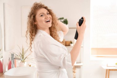 Genç bir kadın banyoda saçına kuru şampuan sürüyor.