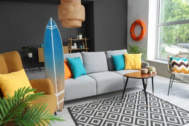 Oturma odasının içinde rahat bir kanepe, koltuk ve sörf tahtası.