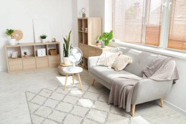 Oturma odasının içinde kanepe ve elektrikli vantilatör var.