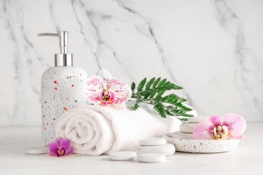 Spa taşları, kozmetik ürünleri, havlu ve orkide çiçekleri açık arkaplanda