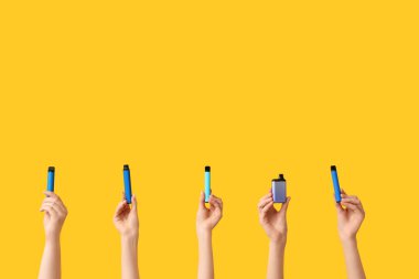 Sarı arka planda elektronik sigaraları tutan bir sürü el var.