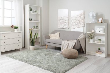 Aydınlık oturma odasının içinde gri kanepe ve raflarda modern elektrikli vantilatör var.