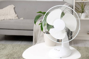 Aydınlık oturma odasındaki kahve masasının üstünde modern elektrikli vantilatör.