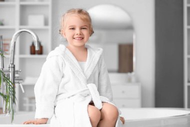 Evdeki küvette oturan bornozlu tatlı küçük kız.