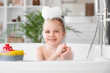 Oyuncak ve köpüklü şirin küçük kız banyoda banyo yapıyor.