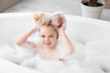 Küvette banyo süngerleriyle oynayan tatlı küçük kız.
