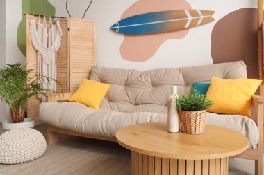 Gri kanepeli, çiçekli, sehpalı ve sörf tahtalı bir oturma odası.