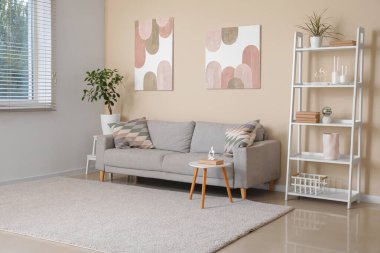 Modern oturma odasının içinde gri kanepe, raf ünitesi, sehpa ve beyaz duvarda resimler.