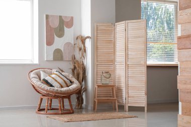 Modern oturma odasının içi rahat koltuğu, vazo dolusu çim, sehpa ve beyaz duvarda resmi olan.