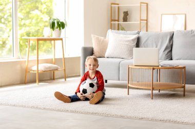 Evde yerde oturan futbol topuyla küçük şirin bir çocuk.