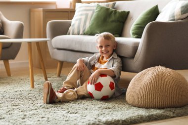 Oturma odasında futbol topuyla yerde oturan sevimli küçük çocuk.