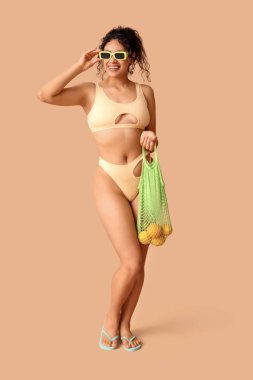 Güzel Afro-Amerikalı bir kadın şık bir mayo giymiş elinde kahverengi arka planda portakallı bir torba tutuyordu.