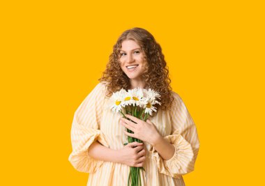 Sarı arka planda bir buket papatya çiçeğiyle mutlu genç kadın.