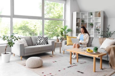 Genç Asyalı kadın evdeki kanepede dizüstü bilgisayar kullanıyor.