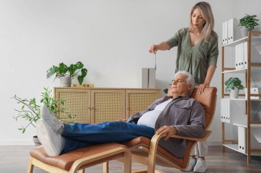 Cep saati olan bir kadın psikolog ofiste olgun bir adamı hipnotize ediyor.