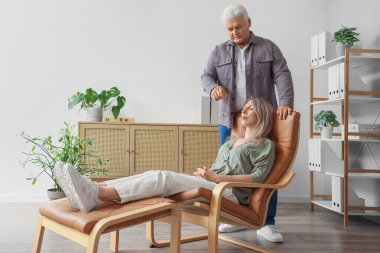 Cep saati olan bir erkek psikolog ofisteki koltukta bir kadını hipnotize ediyor.