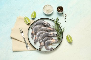 Taze çiğ karides, biberiye ve açık mavi arka planda limon tabağı.