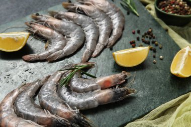 Koyu arkaplanda taze karides, limon ve biberiye.