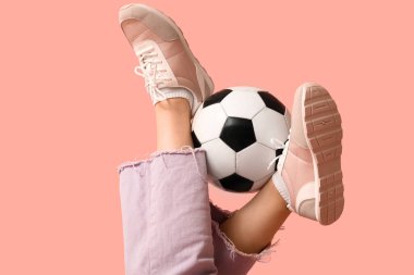 Pembe arka planda futbol topu olan şık spor ayakkabılı genç kadınların bacakları.