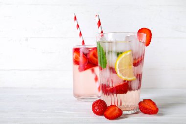 Beyaz ahşap arka planda çilekli ve limonlu taze erimiş su bardakları.