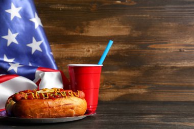 Amerikan bayrağı ve ahşap arka planda kola olan lezzetli bir sosisli sandviç, yakın plan. Amerikan Bağımsızlık Günü kutlamaları