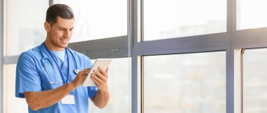 Pencerenin yanında tablet bilgisayarı olan genç bir erkek doktorun portresi. Tasarım için pankart