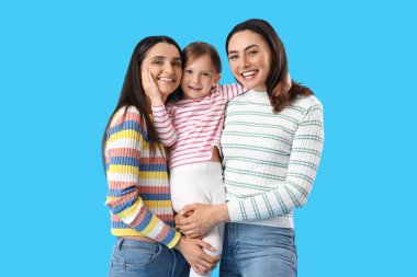 Mavi arka planda evlat edinilmiş küçük kızı kucaklayan genç lezbiyen çift.