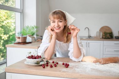 Mutfaktaki masada bir kase kirazlı, oklavalı ve hamurlu güzel bir kadın.