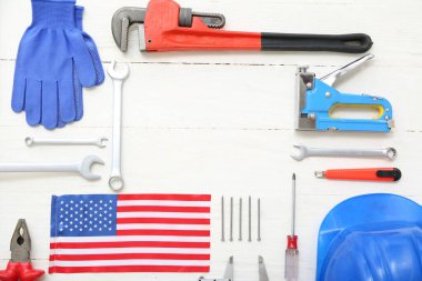 Farklı aletlerden yapılmış çerçeve ve beyaz ahşap arka planda Amerikan bayrağı. İşçi Bayramı kutlamaları