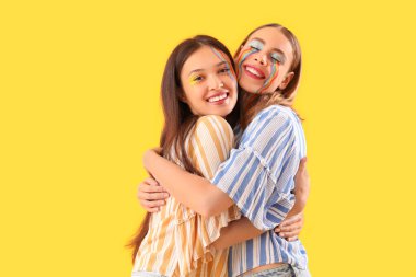 Sarı arka planda sarılan boyalı yüzlü genç kadınlar.