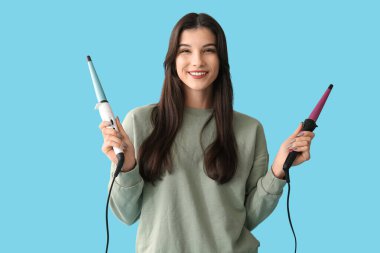 Mavi arka planda saç maşası olan güzel, genç, mutlu bir kadın.